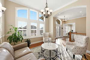 Living room with a chandelier, wood finished floors, ornamental molding, arched walkways, and recessed lighting