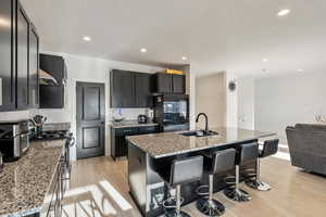 Kitchen featuring dark cabinets, a kitchen bar seating, granite countertops, and gas stove.