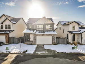 View of front of home with a gate, a garage, concrete driveway, board and batten siding, and stone siding