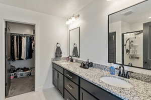 Attached primary bathroom with double vanity, walk in closet, and a standing shower