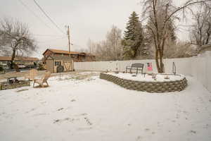 Yard layered in snow featuring an outdoor fire pit, a storage shed, a patio area, and a fenced backyard