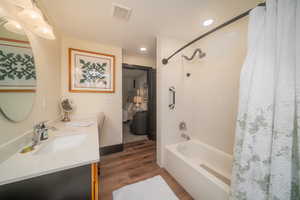 Full bath with shower / tub combo with curtain, double vanity, dark wood-type flooring, connected bathroom, and recessed lighting