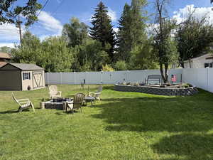 Fenced backyard featuring a fire pit, a patio area, and a storage shed