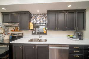 Kitchen with appliances with stainless steel finishes, under cabinet range hood, recessed lighting, and light stone counters