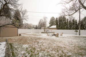 Yard covered in snow with an outdoor fire pit, a fenced backyard, a shed, and a patio