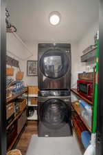 Washroom with stacked washer / dryer and wood finished floors