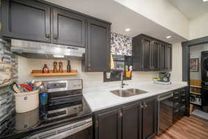 Kitchen featuring stainless steel appliances, estacked washer and dryer, under cabinet range hood, light wood-style flooring, and recessed lighting