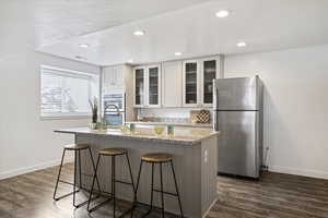 Kitchen featuring appliances with stainless steel finishes, a breakfast bar area, light stone counters, a center island with sink, and glass insert cabinets