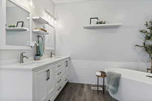 Bathroom featuring double vanity, dark wood-style floors, a freestanding tub, wainscoting, and tile walls