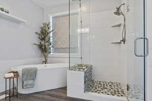 Full bathroom with a shower stall, a freestanding bath, wood finished floors, and tile walls