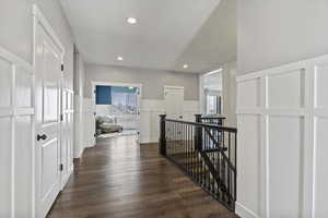 Hall with a decorative wall, a wainscoted wall, an upstairs landing, dark wood-type flooring, and recessed lighting