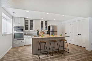 Kitchen featuring a breakfast bar area, light stone countertops, a kitchen island with sink, stainless steel appliances, and white cabinetry