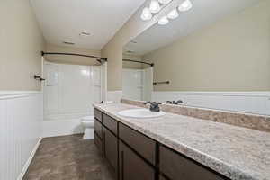Full bath with vanity, wainscoting, washtub / shower combination, and dark stone finish floors