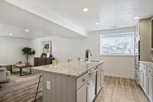 Kitchen with light stone countertops, a kitchen island with sink, a kitchen bar, recessed lighting, and light wood finished floors