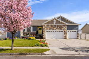 Craftsman-style home featuring an attached garage, concrete driveway, a gate, and stone siding. AI generated spring flowers.