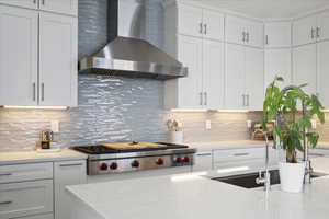 Kitchen with wall chimney exhaust hood, white cabinets, tasteful backsplash, stainless steel gas stovetop, and light stone countertops