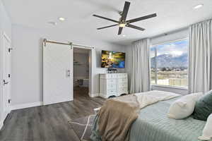Bedroom with a barn door, wood finished floors, connected bathroom, a ceiling fan, and recessed lighting