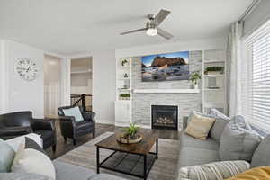Living area with a tile fireplace, wood finished floors, a ceiling fan, and built in shelves