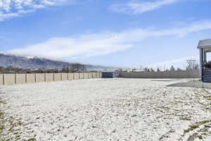 Yard covered in snow featuring a fenced backyard, a storage shed, and a mountain view