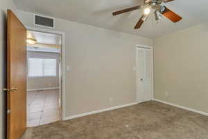 Unfurnished bedroom with carpet floors, a ceiling fan, a closet, and tile patterned floors 890