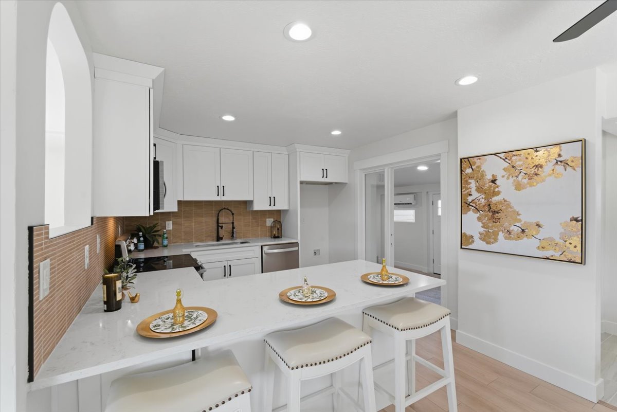 Kitchen featuring a peninsula, a kitchen bar, light stone counters, white cabinetry, and recessed lighting