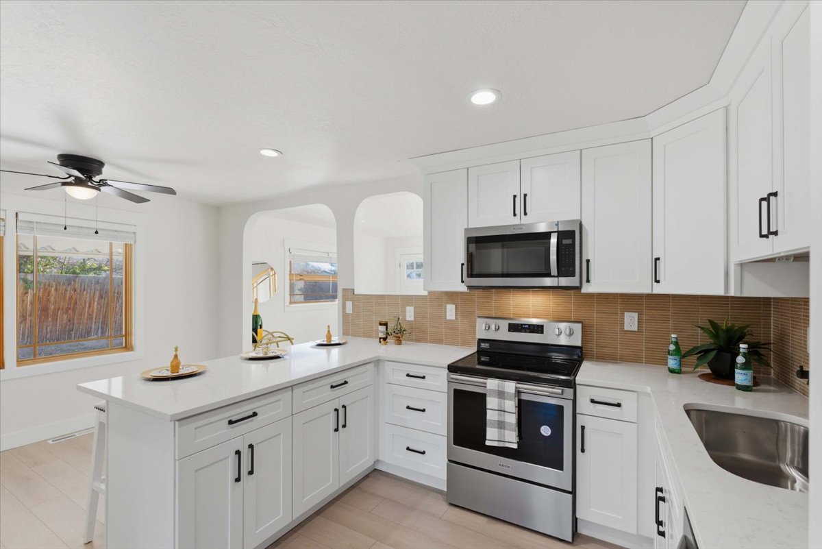 Kitchen with stainless steel appliances, a peninsula, white cabinetry, backsplash, and light stone countertops