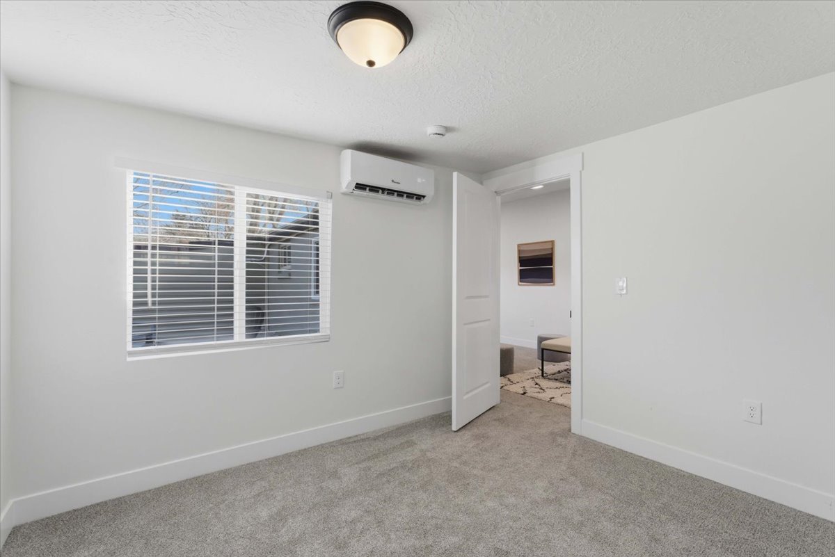 Unfurnished bedroom featuring light colored carpet, a textured ceiling, and a wall mounted AC