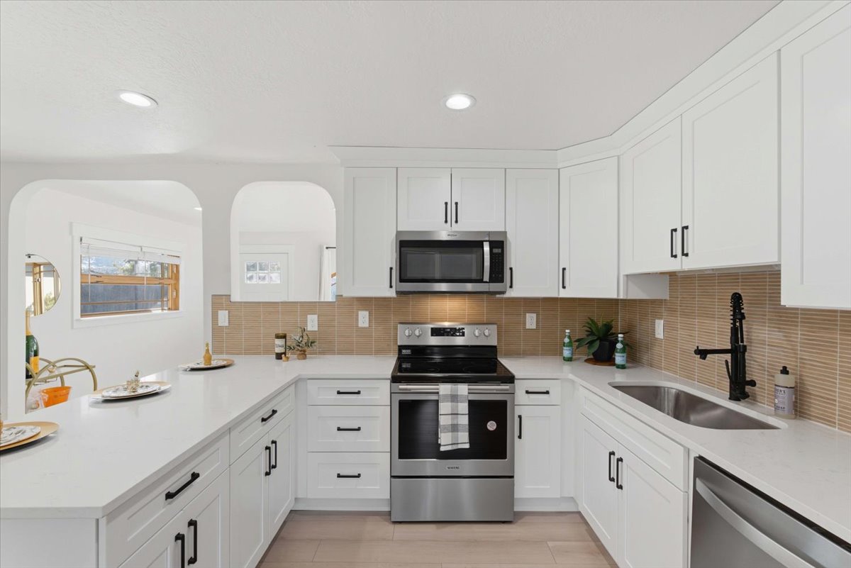 Kitchen with stainless steel appliances, white cabinetry, light stone counters, a peninsula, and recessed lighting