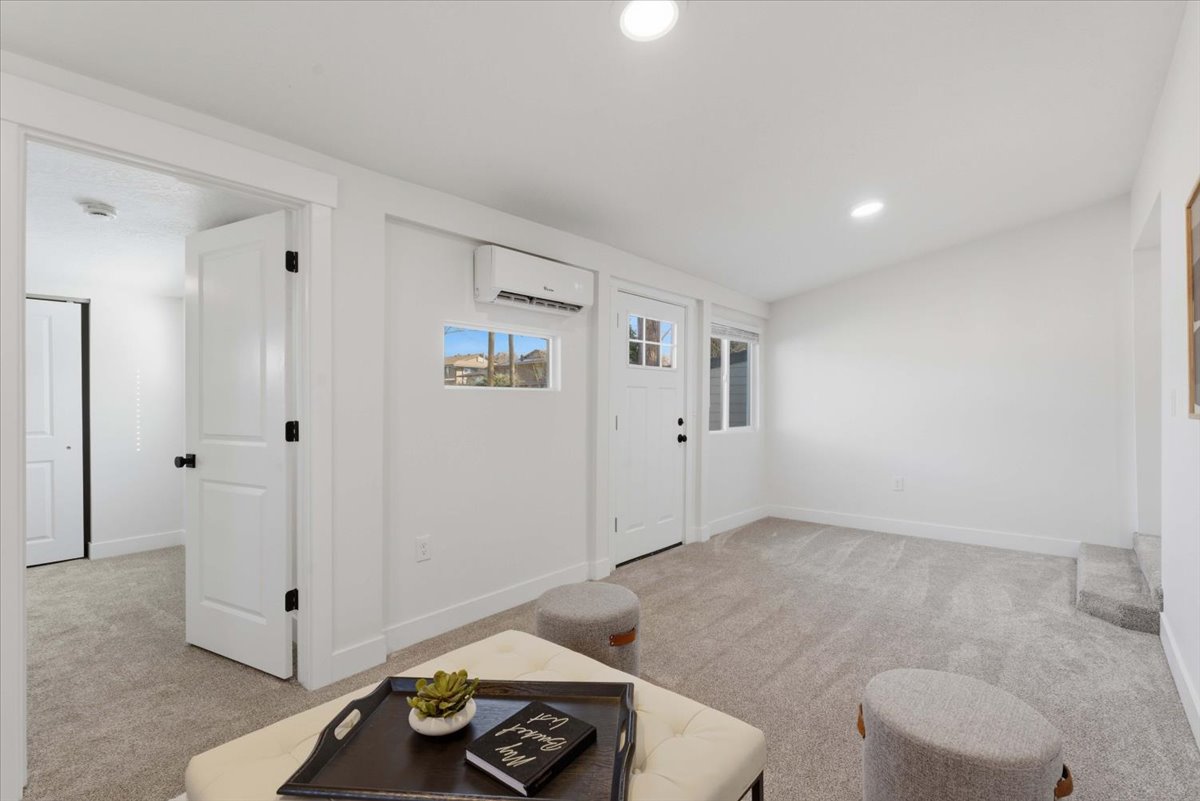 Living room with light colored carpet, recessed lighting, and a wall mounted AC