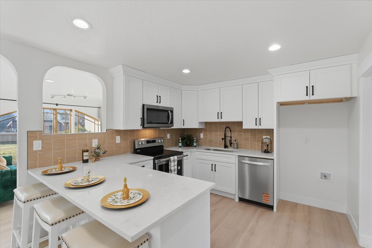 Kitchen featuring appliances with stainless steel finishes, light stone counters, light wood-style flooring, a kitchen breakfast bar, and white cabinetry