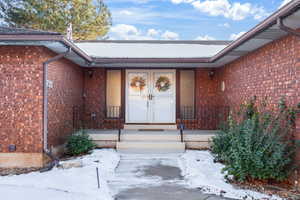 Snow covered property entrance with brick siding, a porch, and french doors