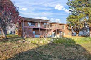 Rear view of property featuring a wooden deck, a lawn, brick siding, stairs, and a patio