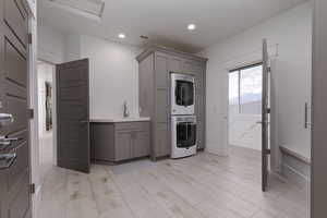 Kitchen featuring gray cabinetry, stacked washer / dryer, light countertops, light wood-style floors, and recessed lighting