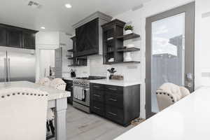 Kitchen featuring open shelves, dark cabinets, stainless steel appliances, a breakfast bar area, and recessed lighting