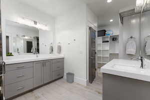 Bathroom with two vanities, a spacious closet, light wood-type flooring, and recessed lighting