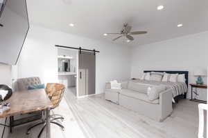 Bedroom with a barn door, recessed lighting, ceiling fan, light wood-style floors, and a desk