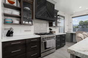 Kitchen with open shelves, stainless steel range, custom exhaust hood, light stone counters, and light wood-type flooring