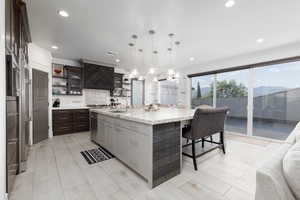 Kitchen featuring a breakfast bar area, glass insert cabinets, pendant lighting, a spacious island, and light stone countertops