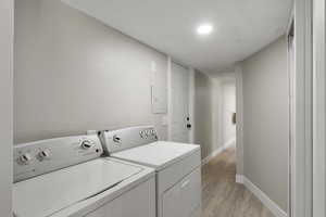 Laundry room featuring light wood-style flooring, washing machine and dryer, and electric panel