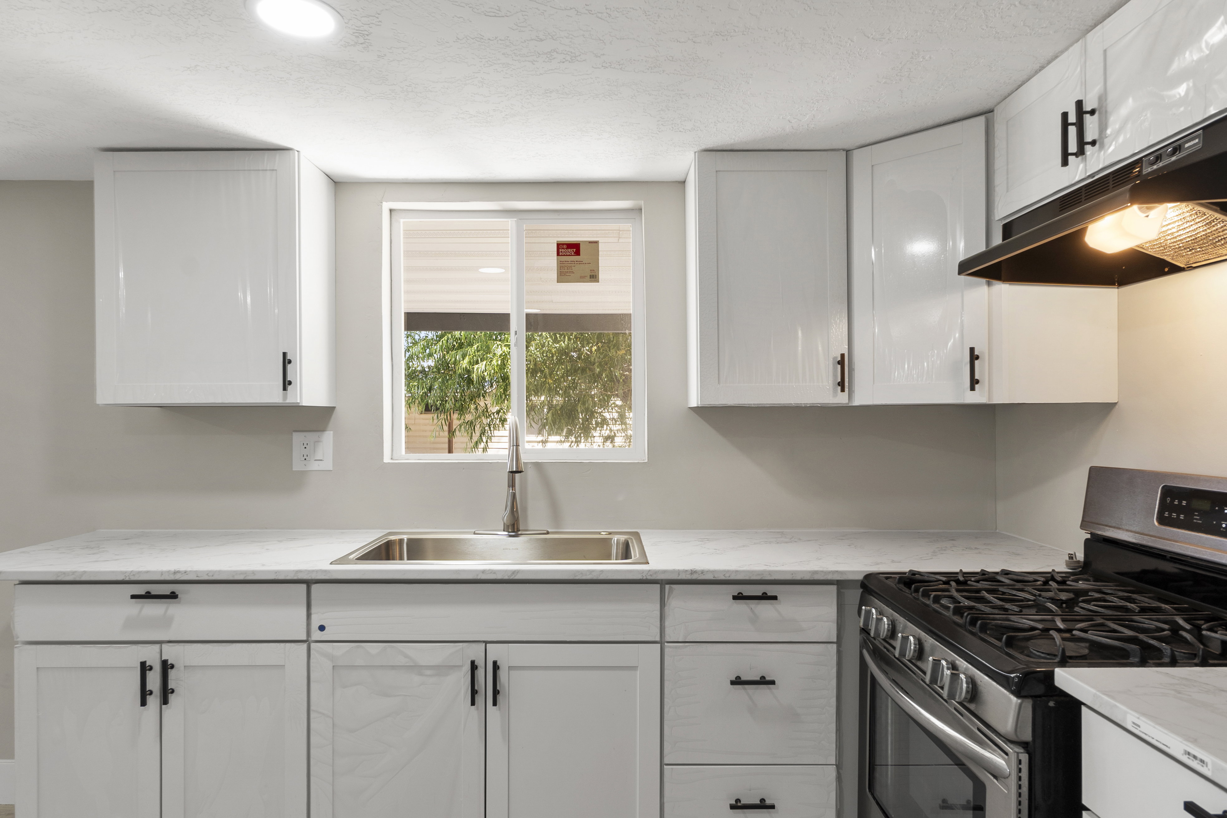 Kitchen with stainless steel gas range oven, white cabinets, under cabinet range hood, light stone countertops, and a textured ceiling