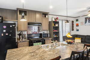 Kitchen featuring black appliances, pendant lighting, under cabinet range hood, crown molding, and tasteful backsplash