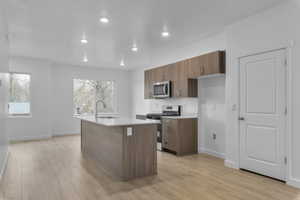 Kitchen with brown cabinets, stainless steel appliances, light wood finished floors, a kitchen island with sink, and recessed lighting