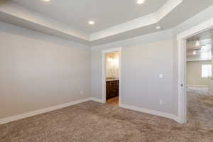 Unfurnished bedroom with a raised ceiling, light colored carpet, ensuite bathroom, and recessed lighting