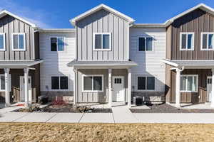 Modern inspired farmhouse with board and batten siding, stone siding, a porch, a shingled roof, and a front lawn
