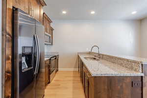 Kitchen with a peninsula, light stone counters, appliances with stainless steel finishes, brown cabinets, and recessed lighting