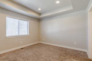 Empty room with a tray ceiling, recessed lighting, and carpet floors