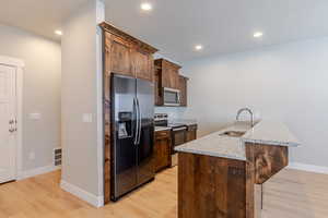 Kitchen featuring stainless steel appliances, light stone countertops, a breakfast bar area, light wood-style flooring, and recessed lighting