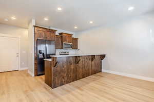 Kitchen featuring a peninsula, refrigerator with ice dispenser, a kitchen bar, light wood-style floors, and light stone countertops