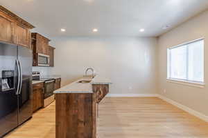 Kitchen featuring stainless steel appliances, light wood-type flooring, light stone countertops, recessed lighting, and a breakfast bar