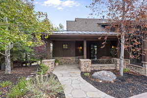 View of front entrance with stone siding, a metal roof, wooded lot and covered porch
